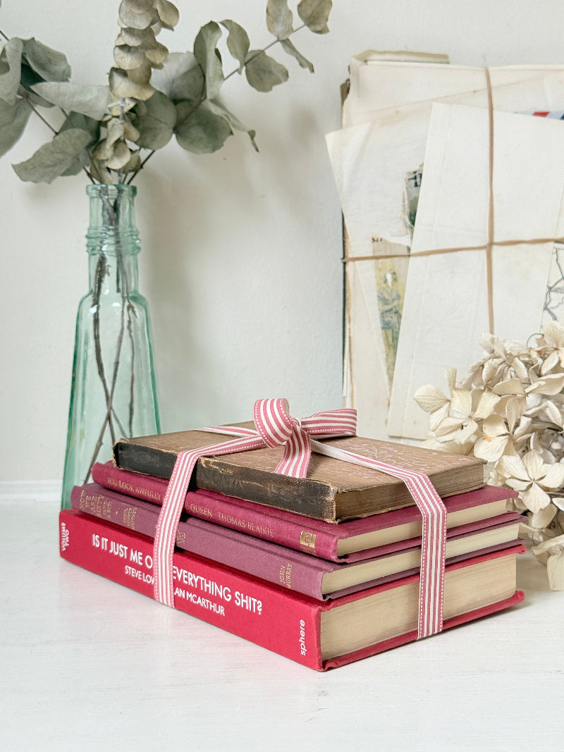 Stack of cloth bound vintage books in red and warm pink tones tied with striped ribbon and dried flowers