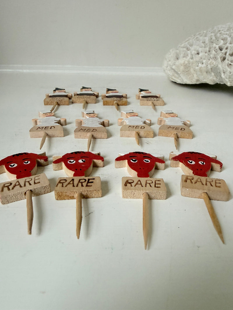 Vintage hand painted wooden steak markers on cocktail sticks labelled rare medium and well done, photographed on a white surface
