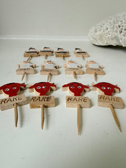 Vintage hand painted wooden steak markers on cocktail sticks labelled rare medium and well done, photographed on a white surface