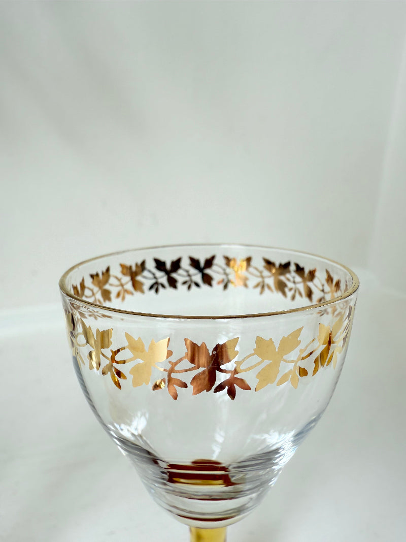 Vintage set of four shot glasses with amber stems and gilt rims, photographed on a white surface