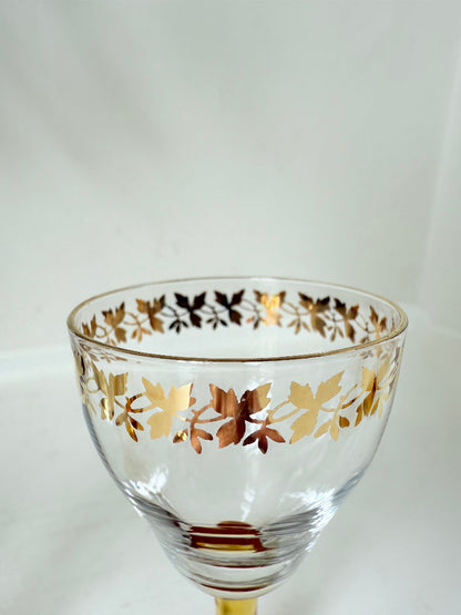 Vintage set of four shot glasses with amber stems and gilt rims, photographed on a white surface
