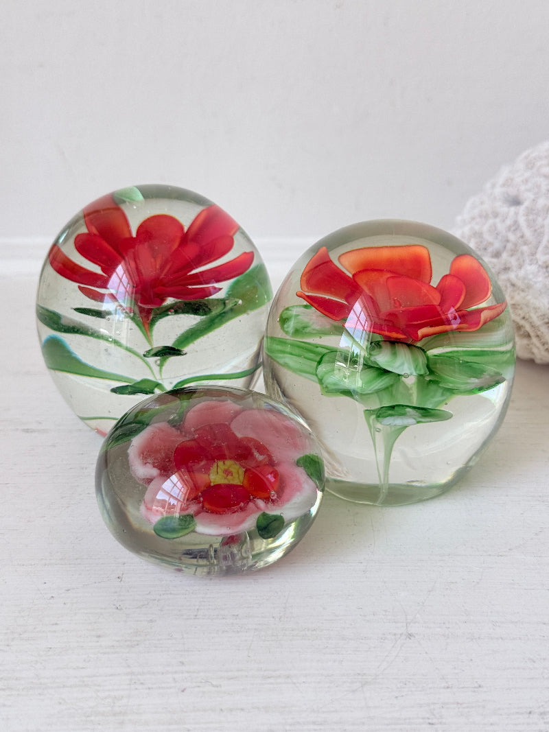 Trio of vintage glass paperweights with hand worked red floral detail, clear glass domes and green leaf decoration