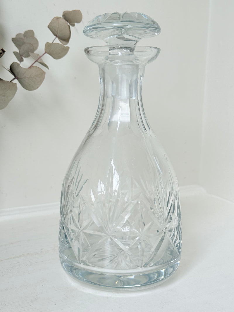 Vintage crystal decanter with faceted stopper and cut glass starburst design, photographed on a white surface