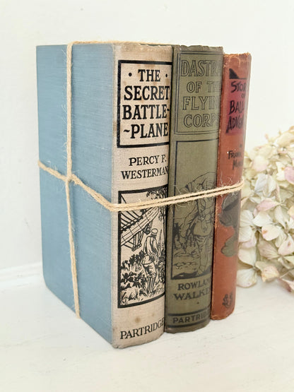 Vintage decorative book bundle in red, olive green and cream tied with twine, photographed on a white surface