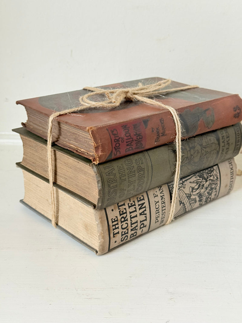 Vintage decorative book bundle in red, olive green and cream tied with twine, photographed on a white surface