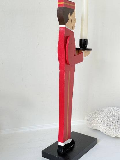 Vintage bellboy candlestick holder in red and black holding a tray with candle, photographed on a white surface