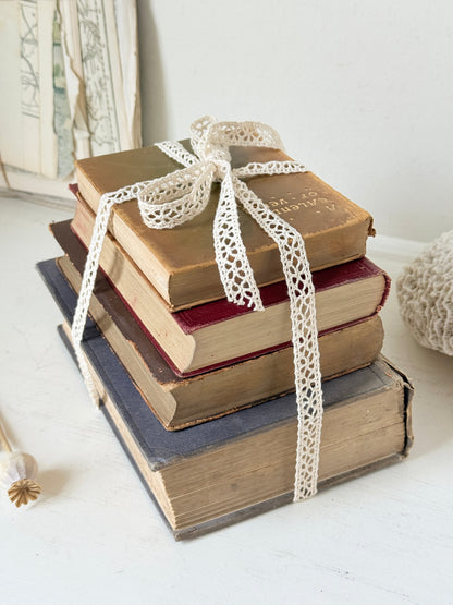 Antique decorative book bundle with faded hardback covers, aged pages and neutral lace tie for vintage interior styling