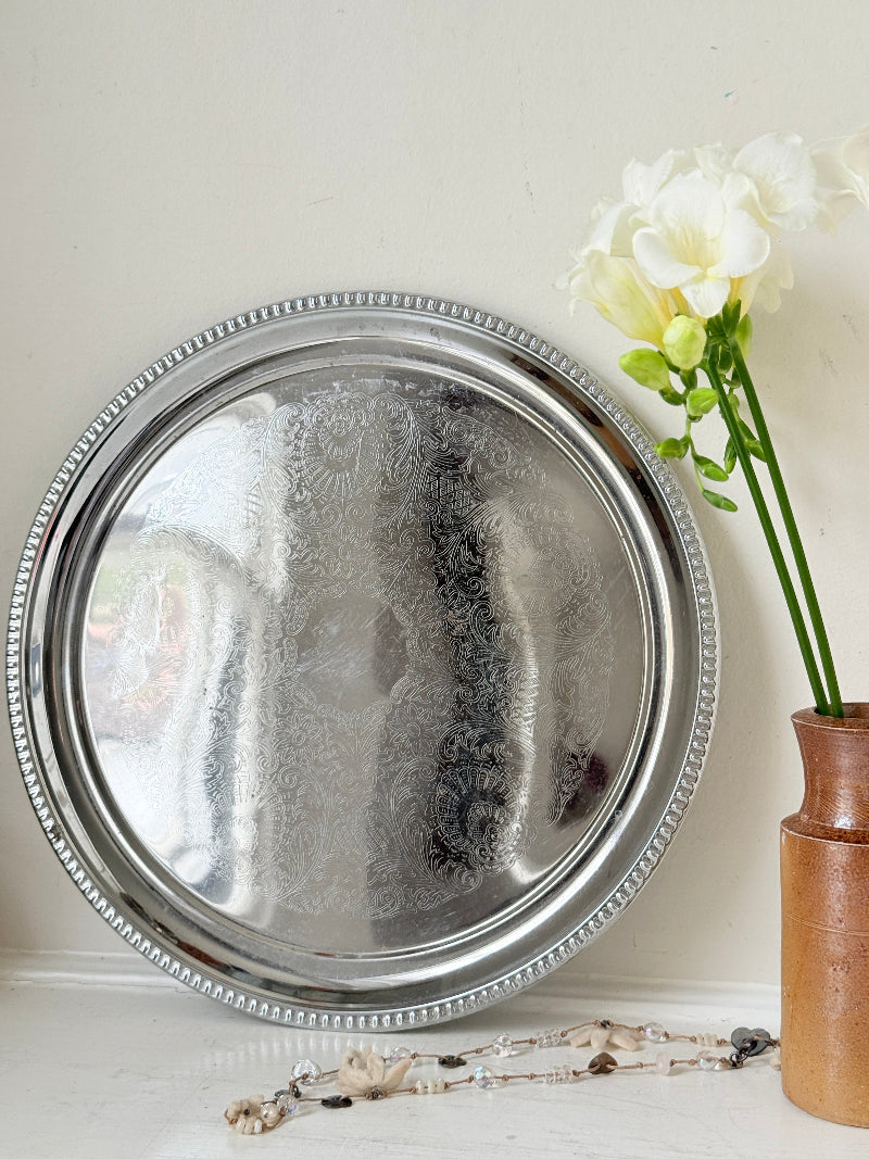 Vintage silver tone round tray with beaded edge, engraved surface detail and reflective finish for drinks or vanity styling