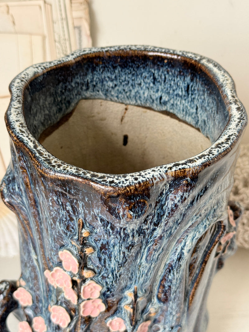 Large ceramic tree trunk vase with applied pink cherry blossom detail, textured bark form and dark drip glaze
