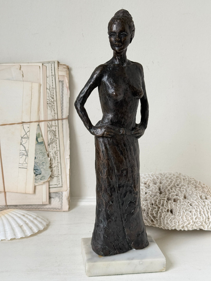 Solid bronze figure of a standing semi nude woman with upswept hair on a white marble base