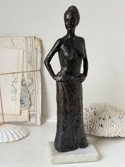 Solid bronze figure of a standing semi nude woman with upswept hair on a white marble base