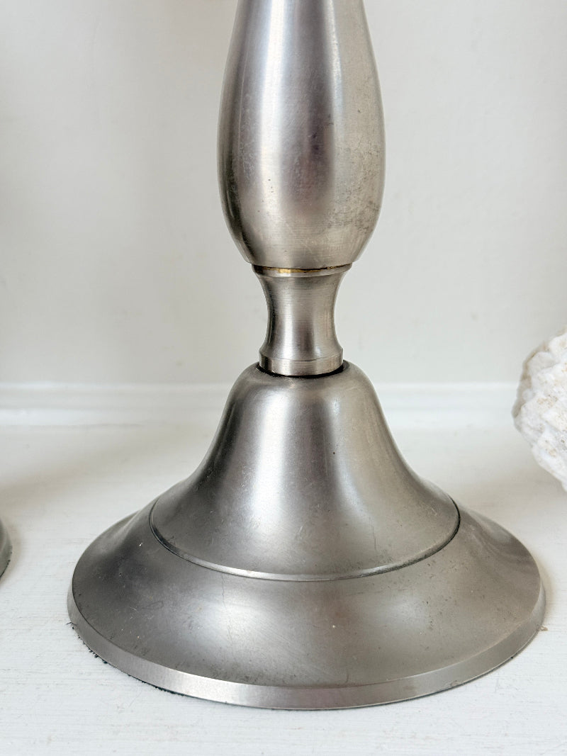 Pair of vintage pewter effect baluster candlesticks with orange taper candles styled on a white surface