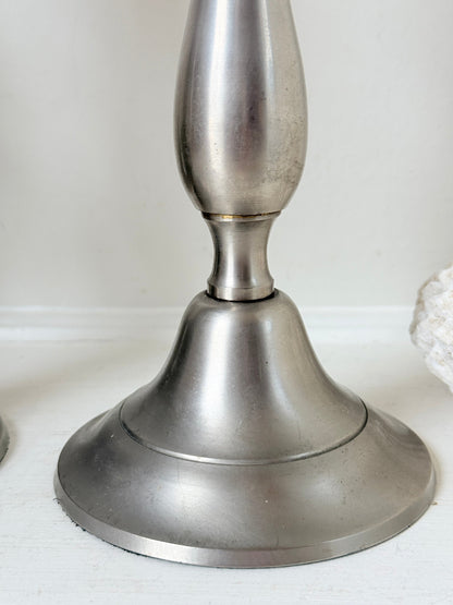 Pair of vintage pewter effect baluster candlesticks with orange taper candles styled on a white surface