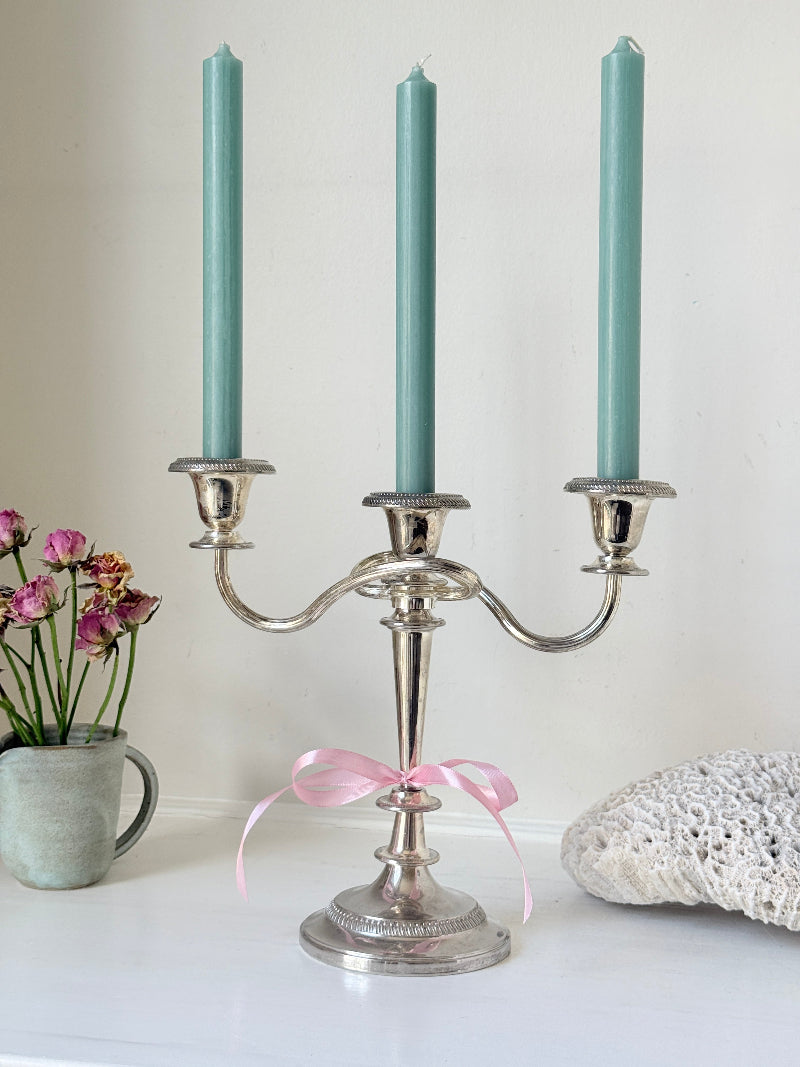 Vintage silver plated three arm candelabra with gadrooned detail and blue green taper candles styled on a white surface