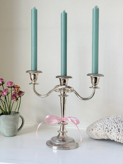 Vintage silver plated three arm candelabra with gadrooned detail and blue green taper candles styled on a white surface
