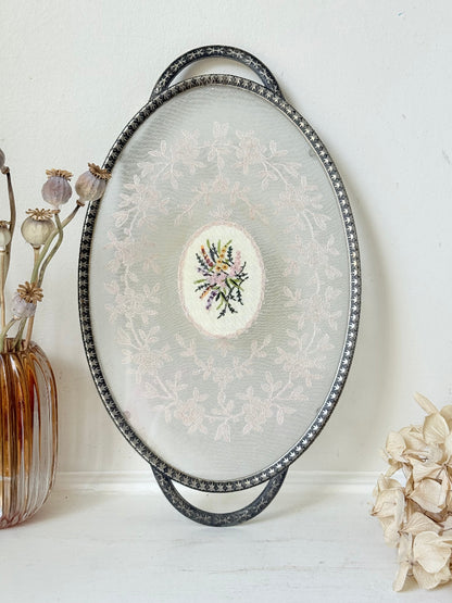 Vintage oval metal tray with pierced gallery sides, twin handles, and floral centre, photographed on white surface.