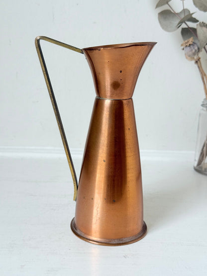 Vintage copper and brass jug with slender handle, photographed on a white surface