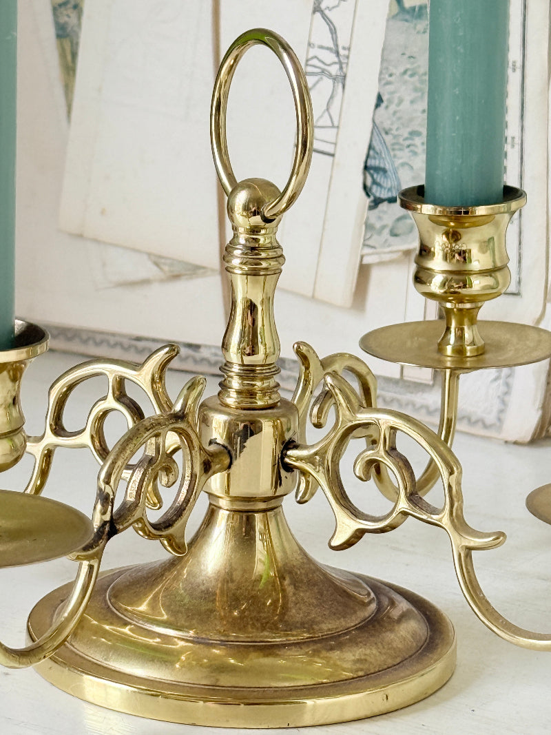 Brass five light candelabra with scrolled arms and a central ring handle on a domed base, photographed on a white surface