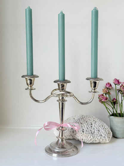 Vintage silver plated three arm candelabra with gadrooned detail and blue green taper candles styled on a white surface