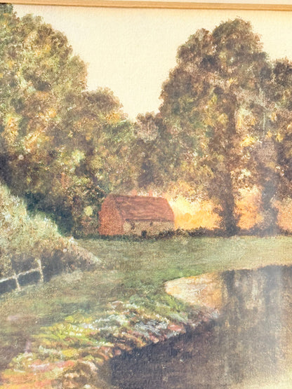 Antique framed rural watercolour of river, trees, and red-roofed building, in dark wooden frame with cream mount, on white surface.