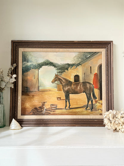 A framed vintage oil painting depicting a brown horse and dog in a stable, displayed on a white mantelpiece with decorative dried flowers and a shell.