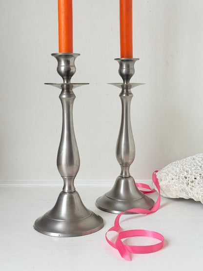Pair of vintage pewter effect baluster candlesticks with orange taper candles styled on a white surface