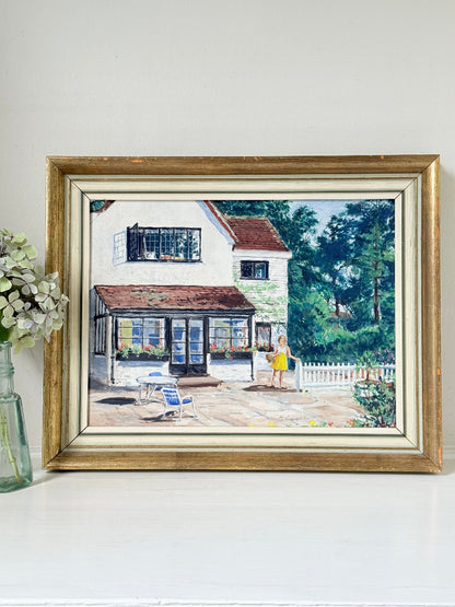 Oil on board painting of a girl in a yellow dress outside a cottage with picket fence, framed, photographed on a white surface