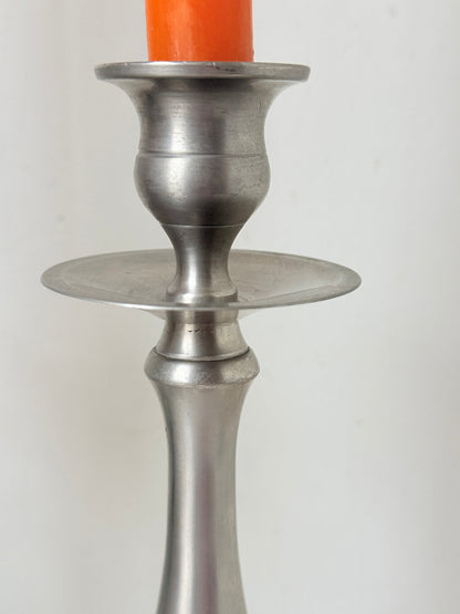 Pair of vintage pewter effect baluster candlesticks with orange taper candles styled on a white surface