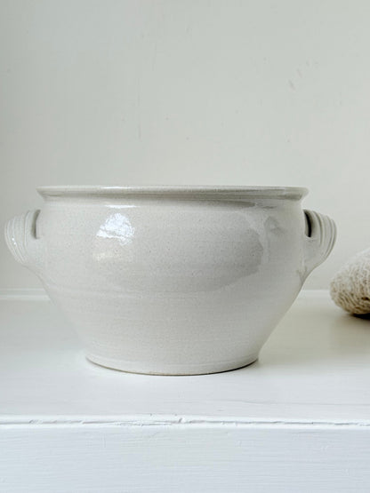 Large studio pottery bowl with hand-painted grape motif and side handles, photographed on a white surface