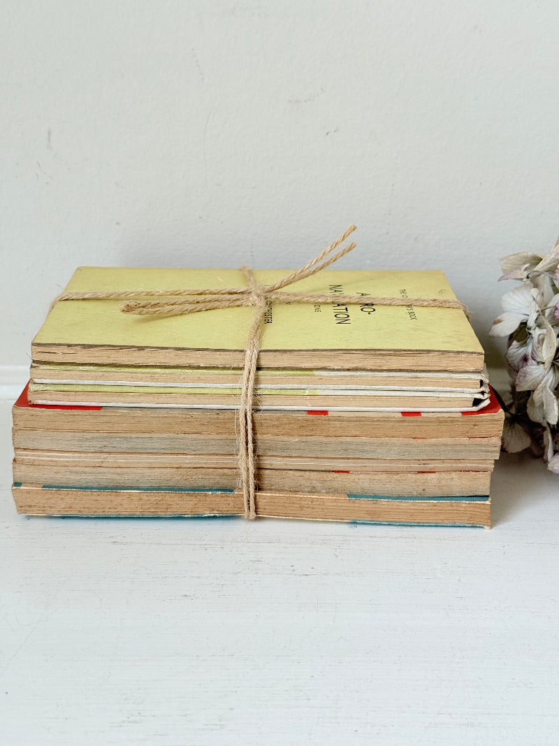 Bundle of vintage Penguin paperback books in orange and cream tones tied with twine, photographed on a white surface
