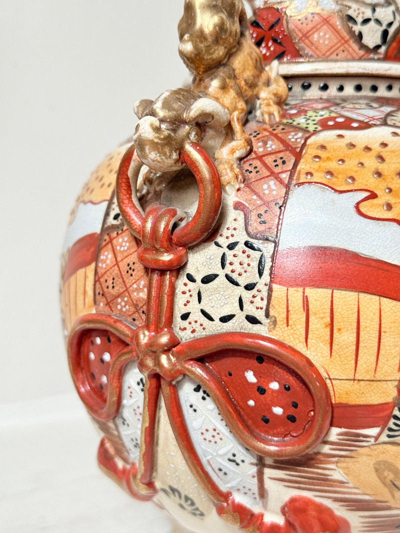 Close-up of a decorative ceramic vessel with a gold-toned lion handle and red, orange, beige, and white patterned glaze.