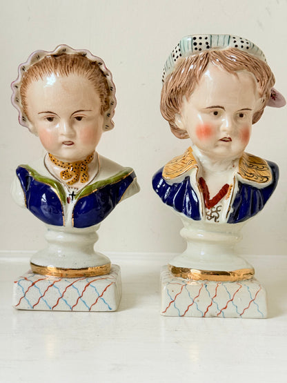 Hand painted Victorian Staffordshire ceramic children busts on white surface, photographed beside dried stems.