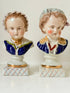 Hand painted Victorian Staffordshire ceramic children busts on white surface, photographed beside dried stems.