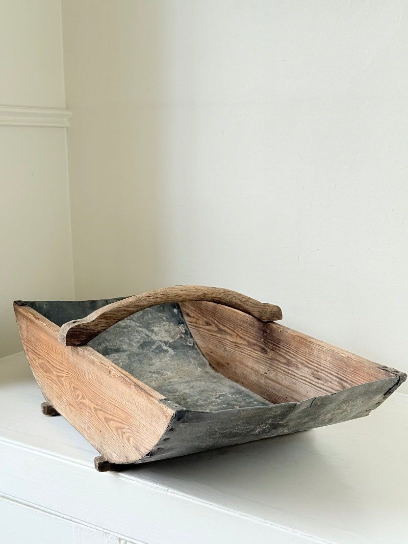Vintage zinc and wood garden trug with arched wooden handle photographed on a white surface
