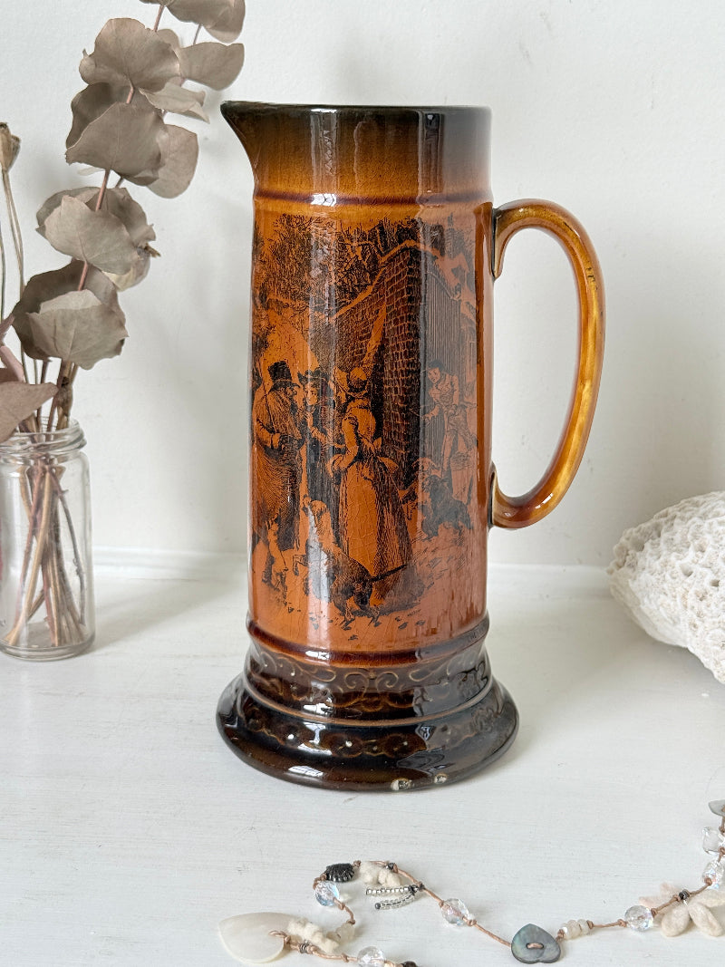 Antique Ridgways stoneware jug photographed on a white surface in amber treacle glaze with A Christmas Visitor black transfer scene and tall handle