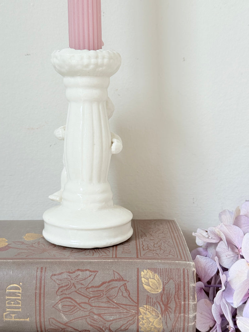 Vintage ceramic candlestick with angel figure and fluted column, cream glazed, styled with pink candle on white surface