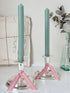 Pair of silver tone candlesticks with wide round stepped bases holding green candles, photographed on a white surface