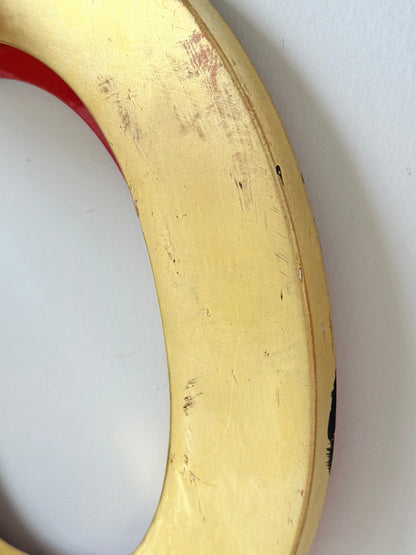A close-up of a circular object, likely a stool or chair leg, featuring a distressed yellow-gold painted finish with visible scratches and wear, set against a plain white wall.