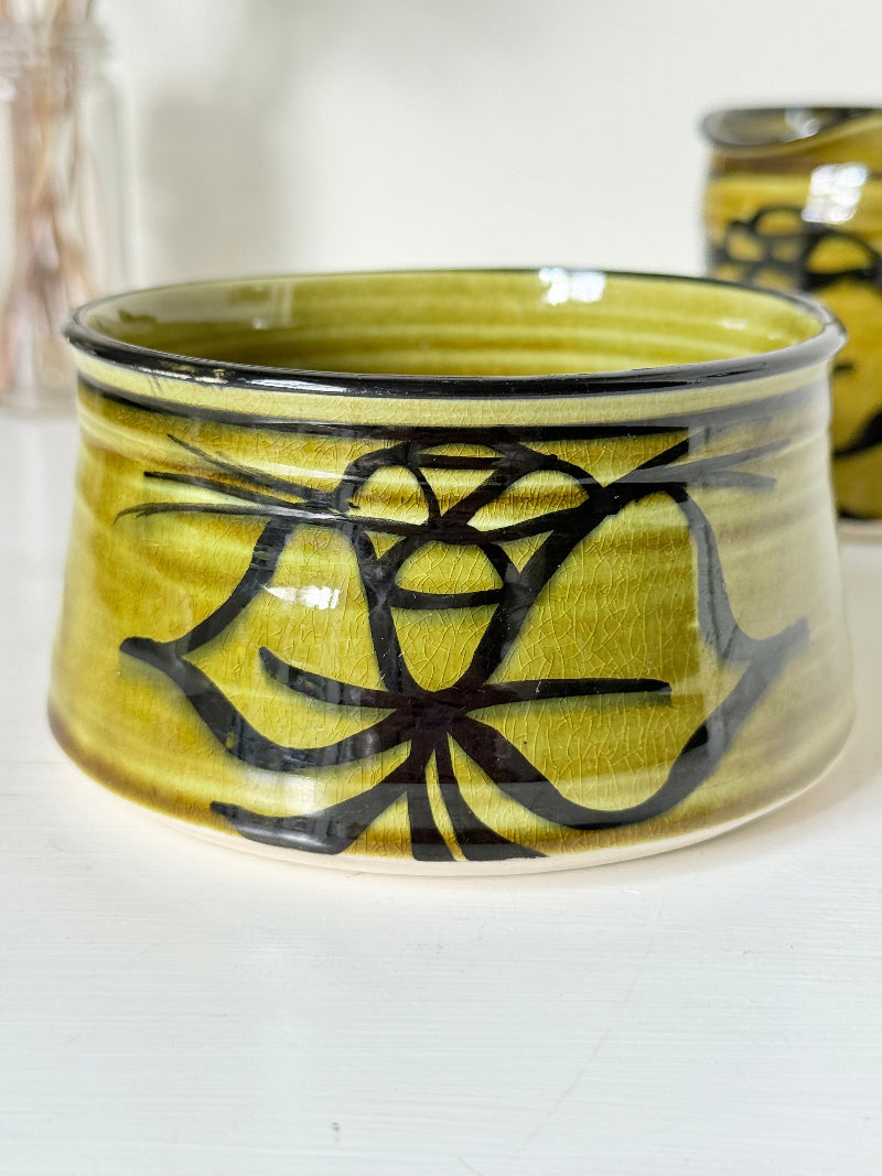 Studio pottery sugar bowl and milk jug in olive green glaze with black brushstroke decoration, photographed on a white surface.