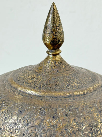 Indian Benares brass lidded jar with pointed finial and darkened interior, photographed on a white surface