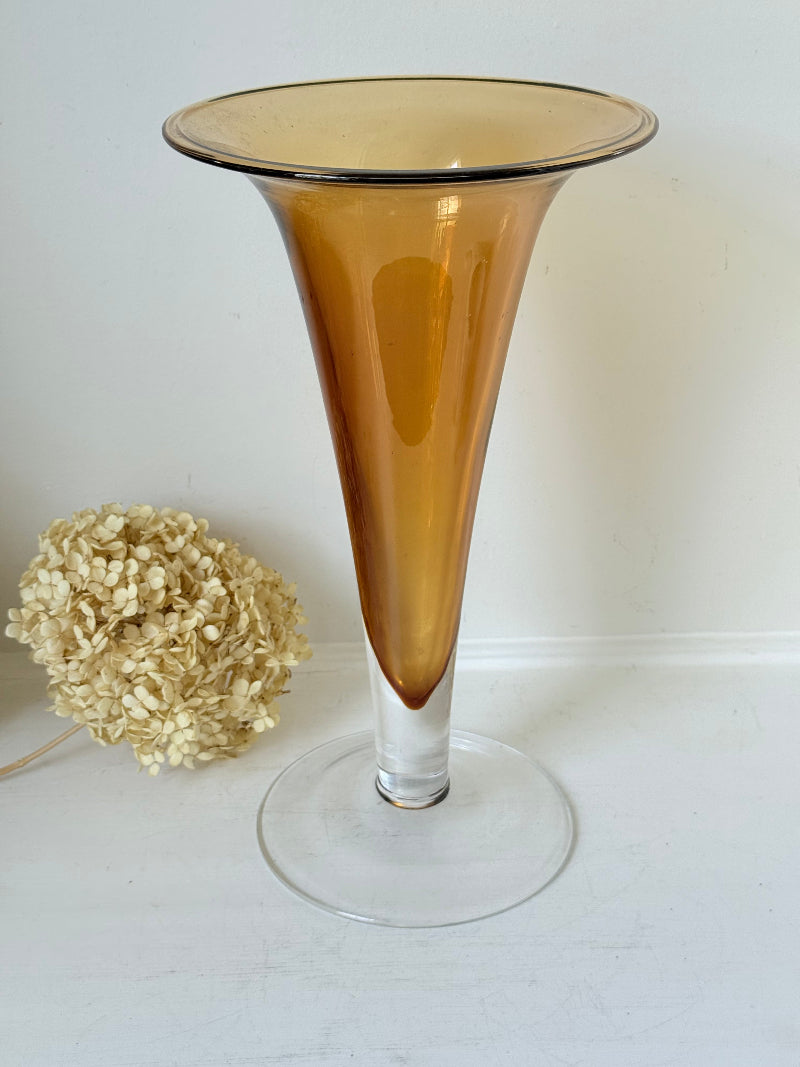 Tall mid-century amber trumpet vase with flared rim and clear glass foot, styled against a neutral background