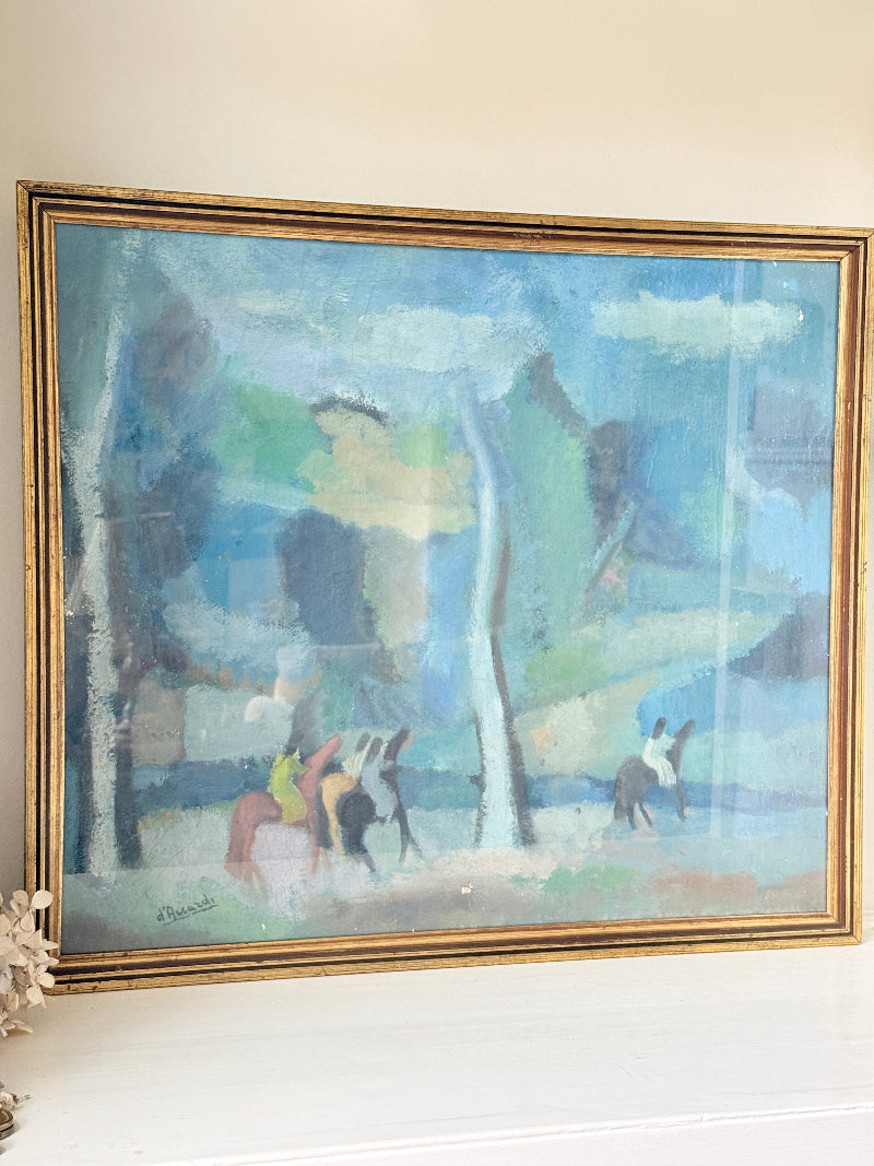 A framed impressionist-style painting depicting a landscape with trees and riders on horseback, housed in a distressed gold frame and leaning against a light beige wall.