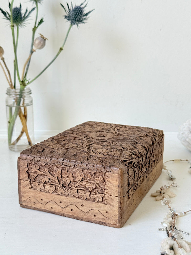 Vintage hand carved wooden jewellery box with floral detail and red fabric lining, photographed on a white surface