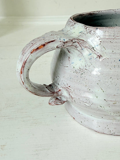 Studio pottery milk jug with soft pink and grey speckled glaze, photographed on a white surface