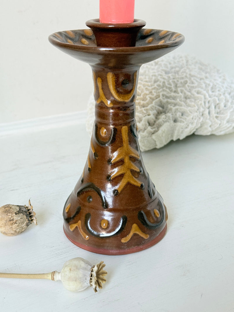 Vintage studio pottery candlestick in brown glaze with cut out decoration styled with coral taper candle on white surface
