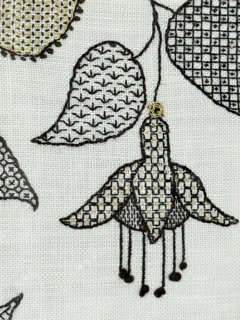 Framed circular hand embroidery of birds and fuchsia flowers in black and grey on white linen, set in gold frame, white surface background.