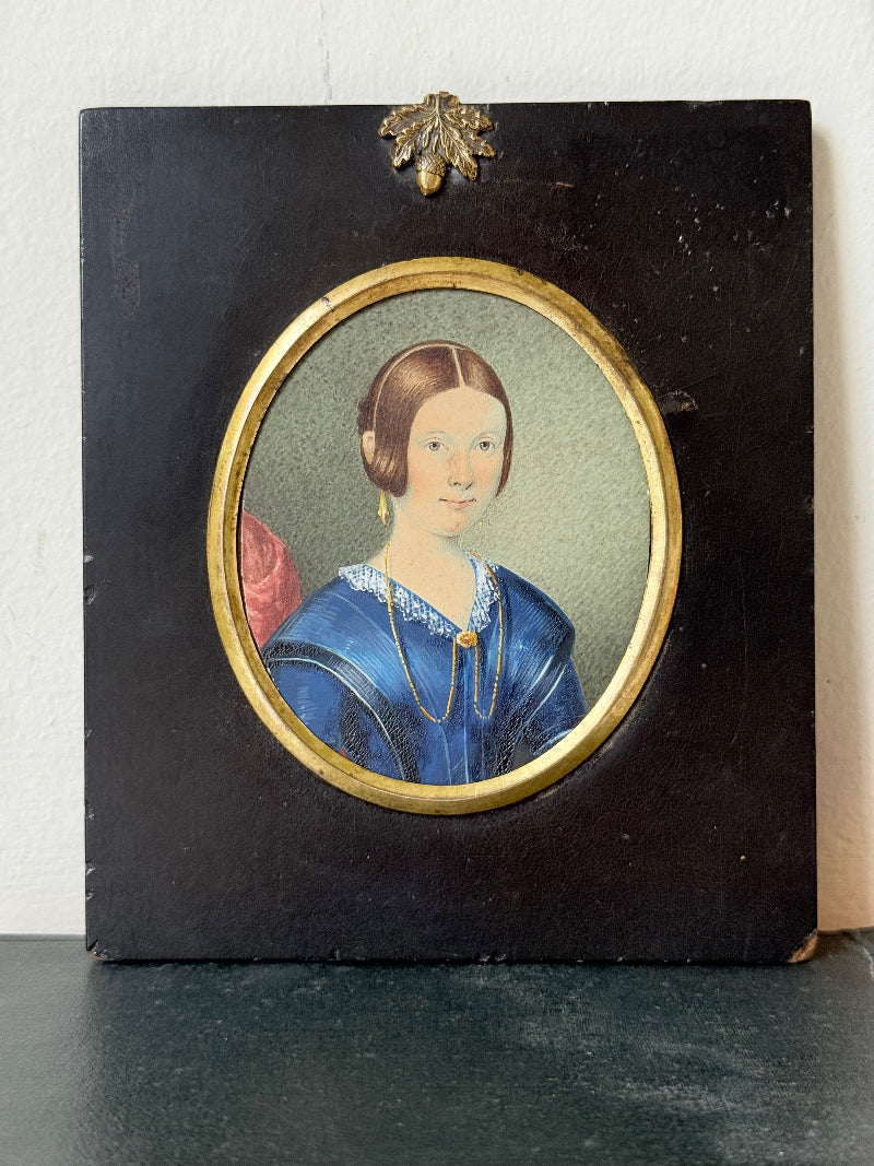 19th century watercolour miniature portrait of woman in blue dress, oval ebonised frame, styled on white background
