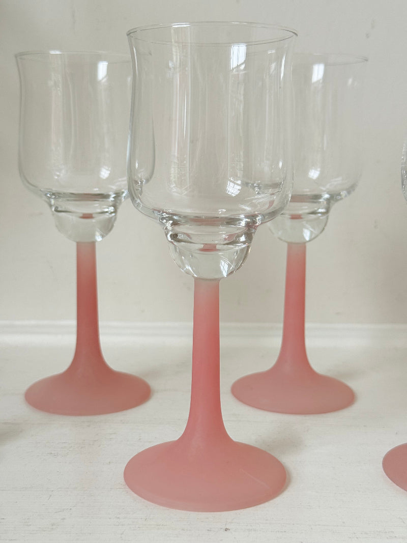 Set of five vintage wine glasses with clear bowls and pink stems photographed on a white surface.