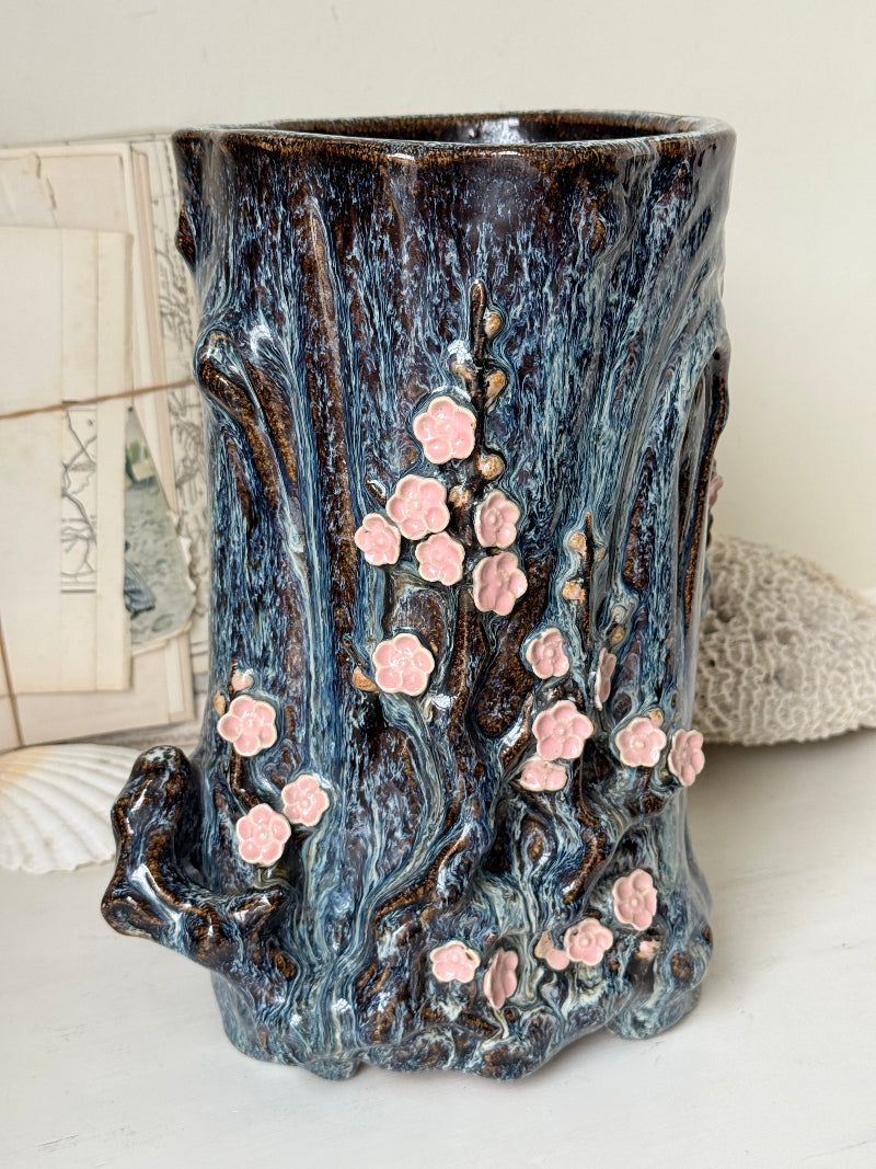Large ceramic tree trunk vase with applied pink cherry blossom detail, textured bark form and dark drip glaze