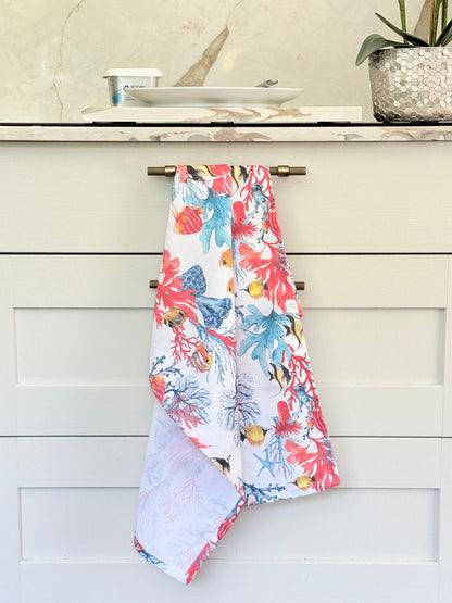 Coral reef print cotton tea towel in crisp white with colourful coral and tropical fish motifs, photographed indoors